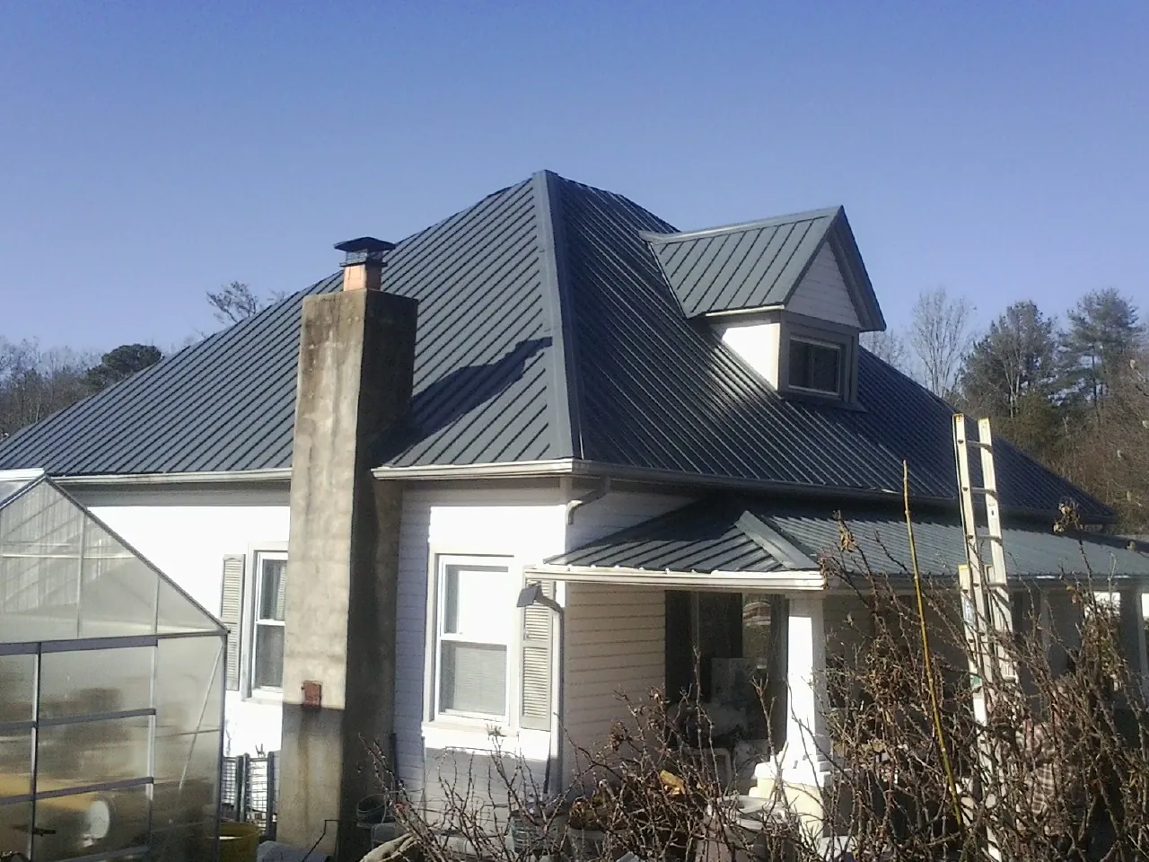 Dark blue standing seam metal roof on a white farmhouse with dormer — Slate & Tile Roof Repair by Roofing Brothers in Latonia