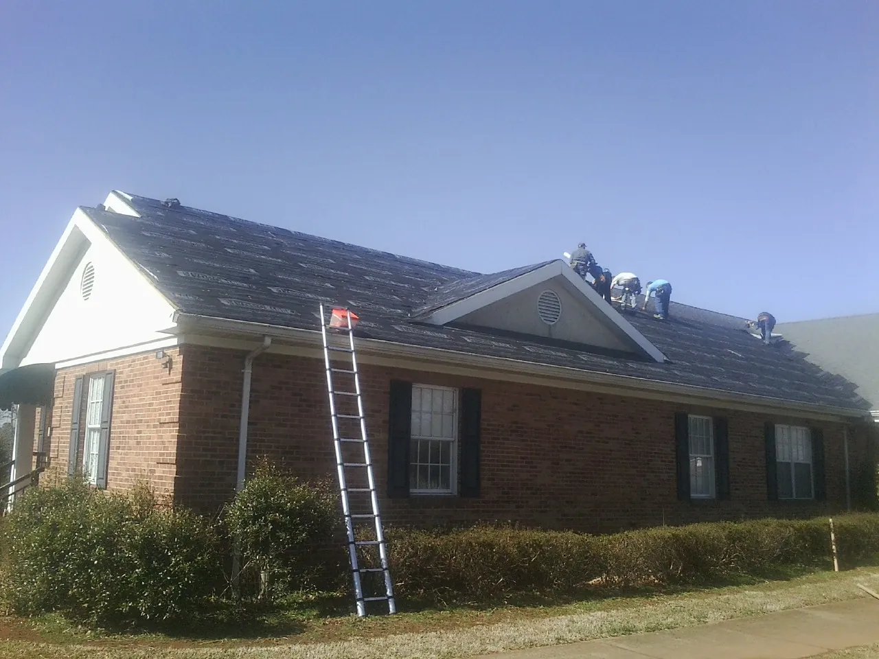Crew tearing shingles off a brick ranch roof with a ladder set — Metal Roof Repair work by our crew in Latonia