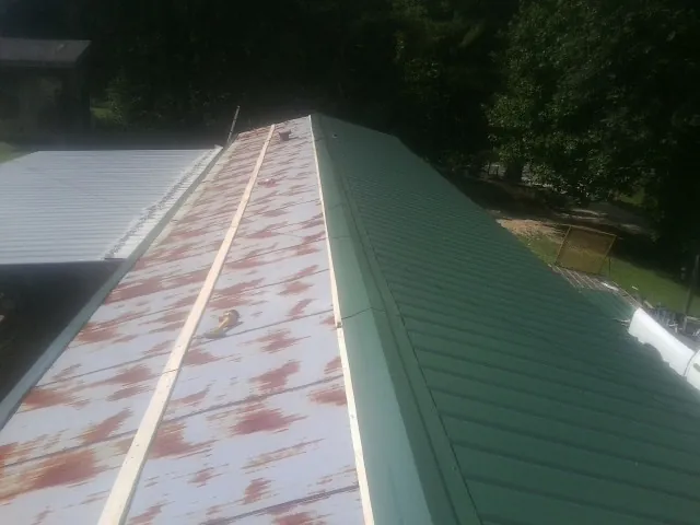 Old rusted panels beside newly installed green metal roofing — Wind Damage Roof Repair by Roofing Brothers in Latonia