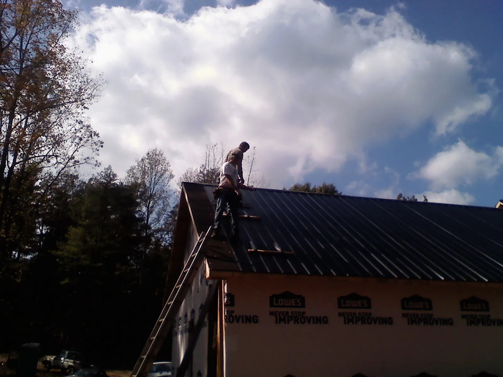 Roofer fastening dark metal panels high against a cloudy sky, from a Roof Inspection job in Latonia