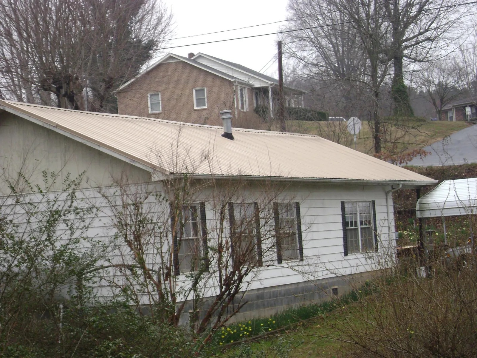 Tan metal roof on a white sided house set into a hillside — Commercial Roofing by Roofing Brothers in Latonia